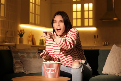 Surprised woman eating popcorn while watching TV on sofa at home