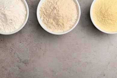 Bowls with different types of flour on grey background, top view. Space for text