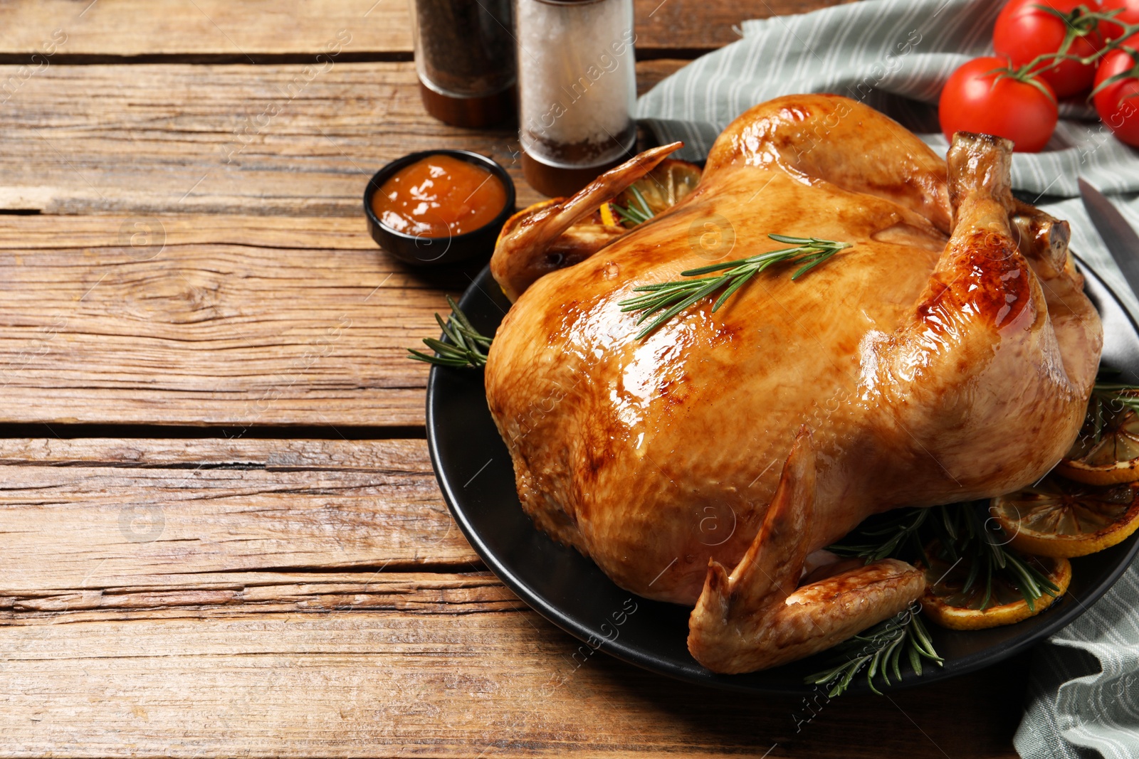Photo of Tasty roasted chicken with rosemary, sauce and lemon on wooden table, space for text