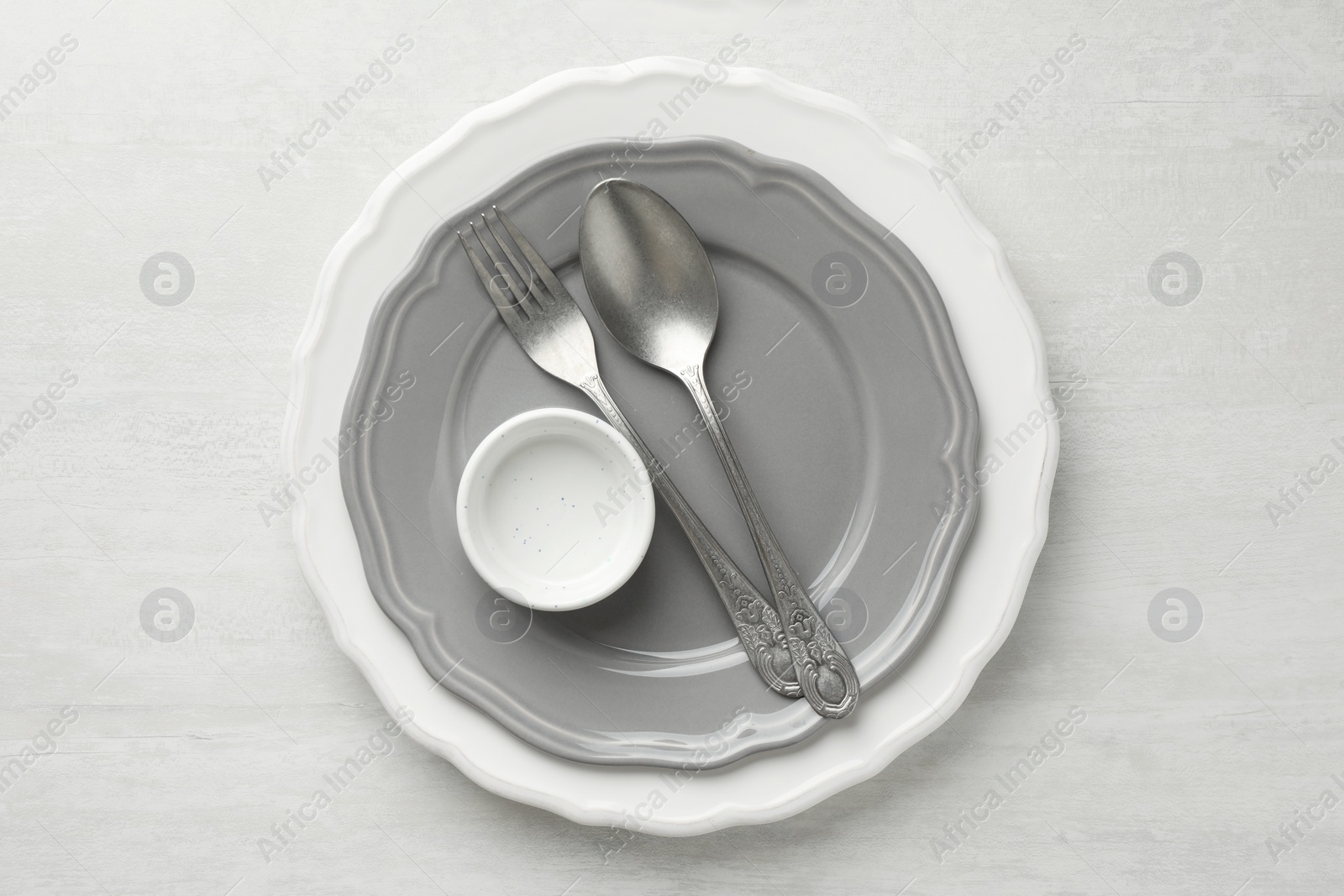 Photo of Stylish setting with cutlery, bowl and plates on light textured table, top view