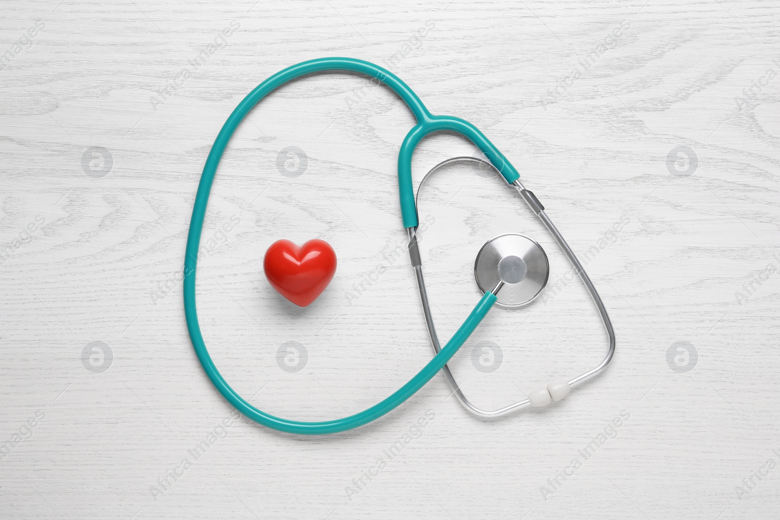 Photo of Stethoscope and red heart on white wooden table, flat lay. Cardiology concept