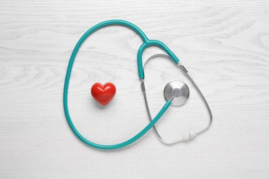 Photo of Stethoscope and red heart on white wooden table, flat lay. Cardiology concept
