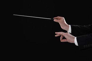 Professional conductor with baton on black background, closeup. Space for text