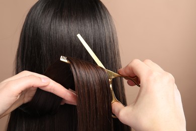 Hairdresser cutting client's hair with scissors on beige background, closeup