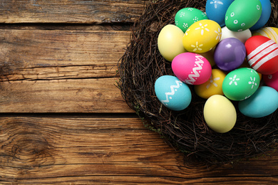 Photo of Colorful Easter eggs in decorative nest on wooden background, top view. Space for text