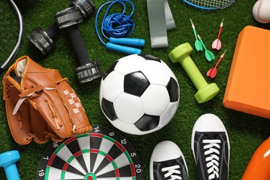 Different sports equipment on green grass, flat lay