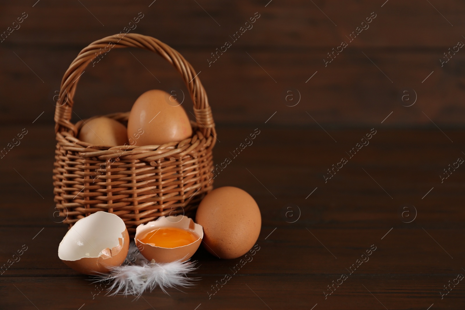 Photo of Raw chicken eggs and feather on wooden table. Space for text