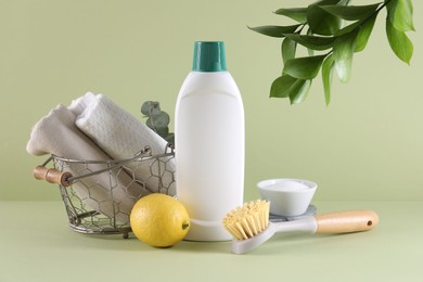 Bottle of cleaning product, baking soda, lemon and brush on light green background