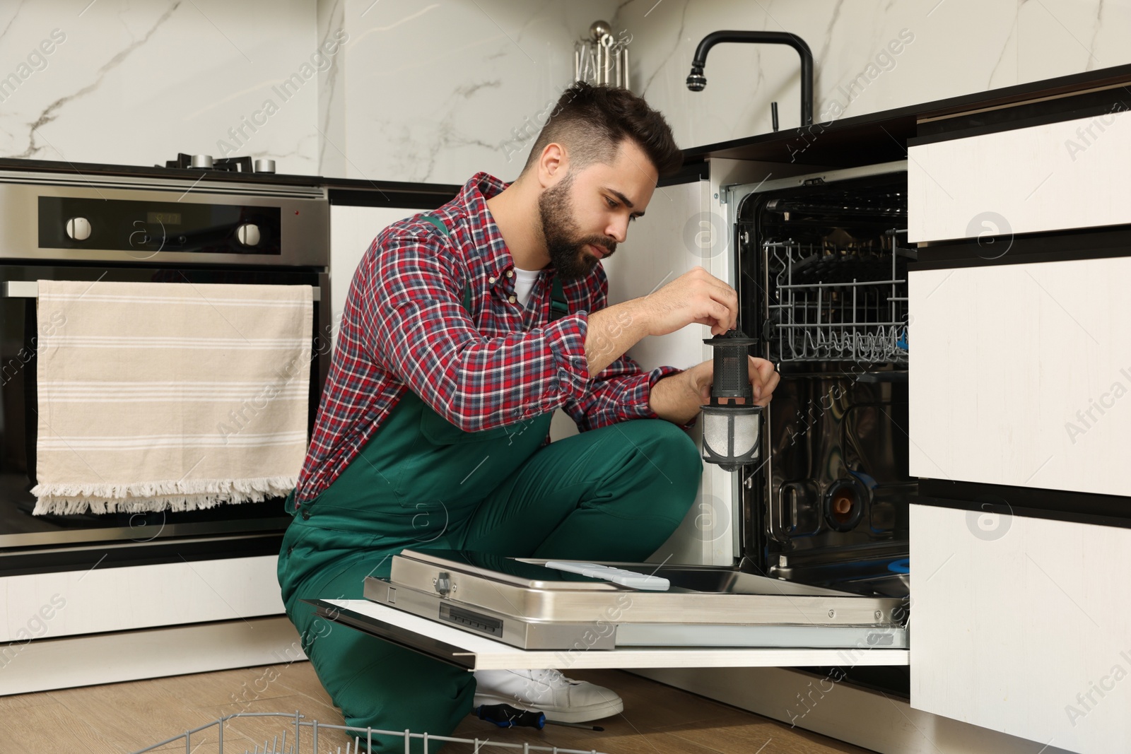 Photo of Repairman holding drain filter near dishwasher in kitchen