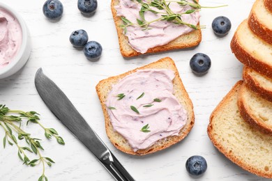 Tasty sandwiches with cream cheese, thyme and blueberries on white wooden table, flat lay