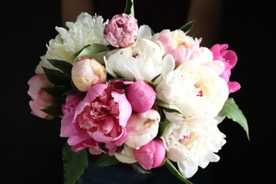 Woman with bouquet of beautiful peonies on black background, closeup