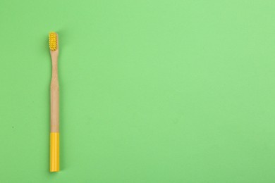 Natural bamboo toothbrush on green background, top view. Space for text