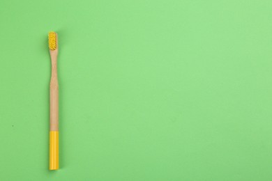 Photo of Natural bamboo toothbrush on green background, top view. Space for text