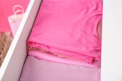 Photo of Many folded pink clothes in white chest of drawers indoors, closeup