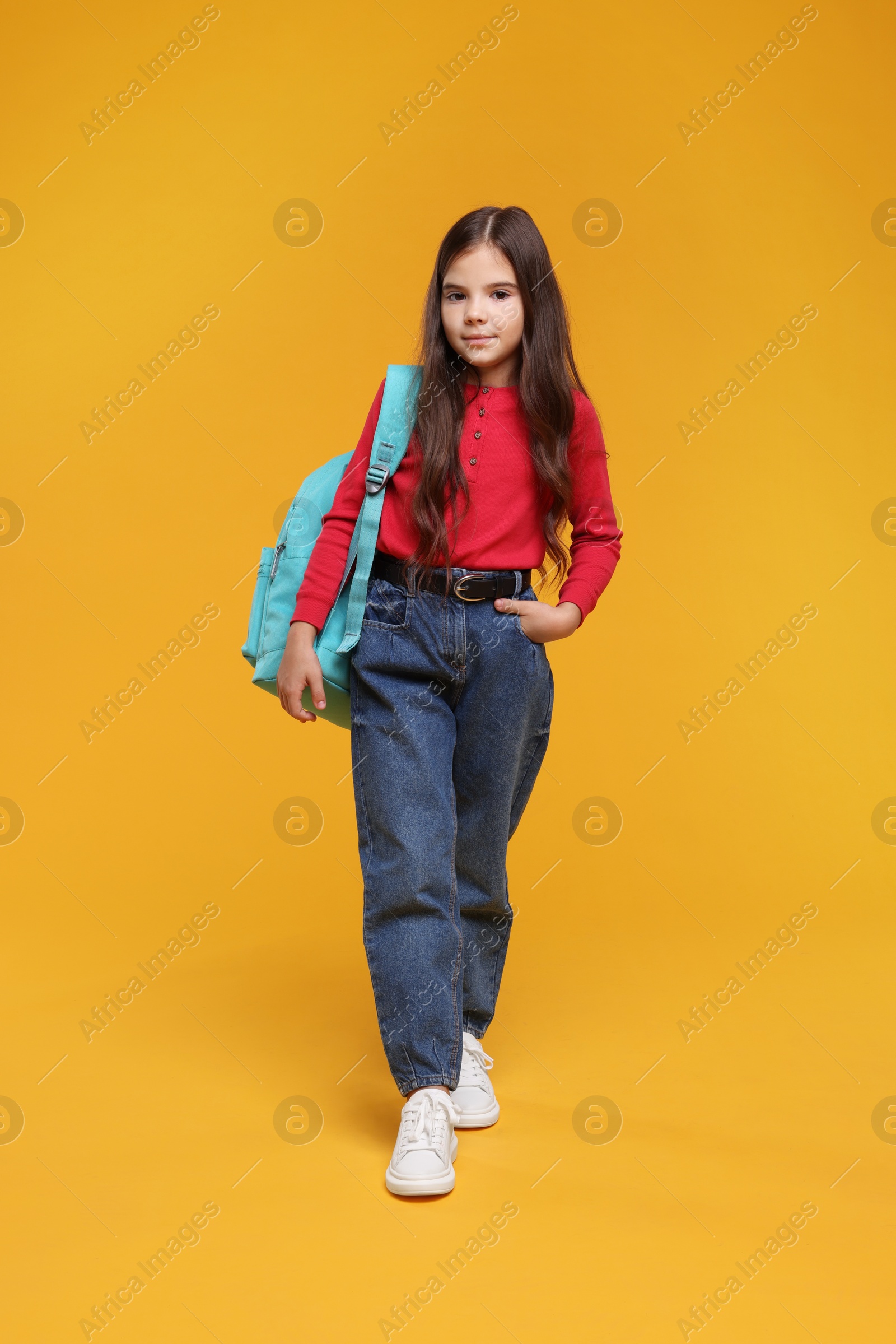 Photo of Back to school. Cute girl with backpack on orange background