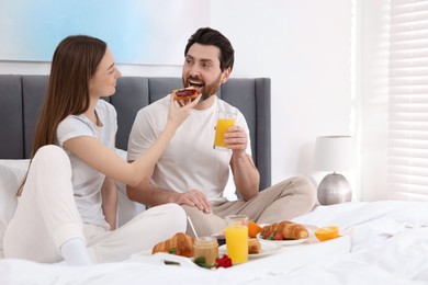Tasty breakfast. Wife feeding her husband on bed at home. Space for text