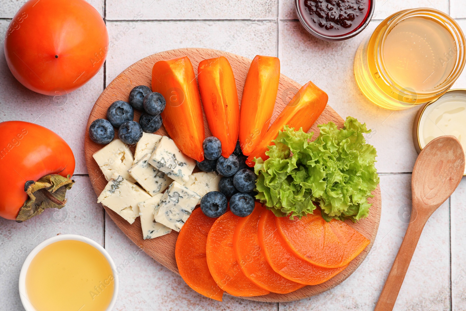 Photo of Delicious persimmon, blue cheese and blueberries on tiled surface, flat lay