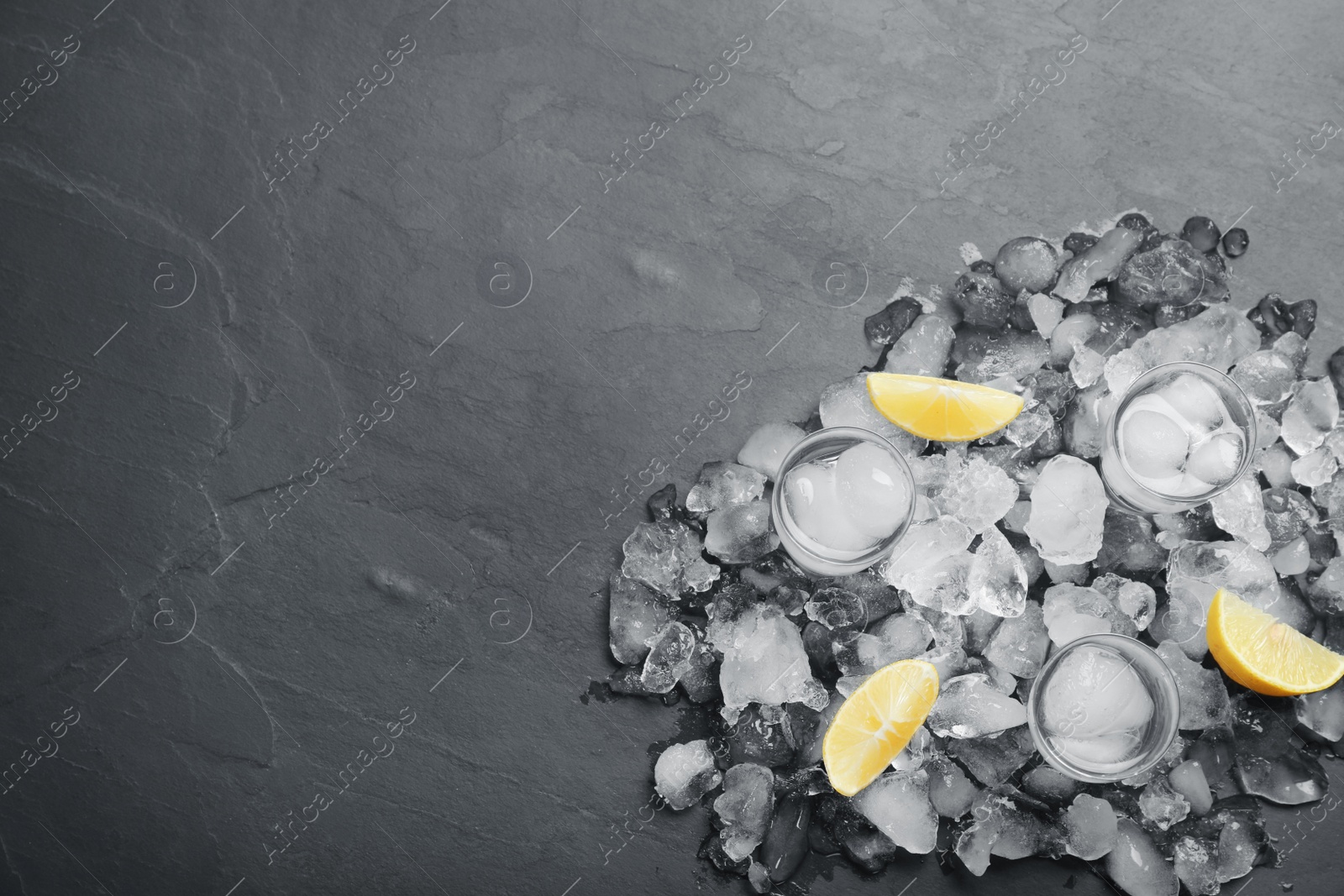 Photo of Shot glasses with vodka, ice and lemon on grey table, flat lay. Space for text