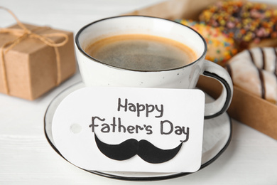 Photo of Tag with phrase HAPPY FATHER'S DAY and coffee on white table, closeup
