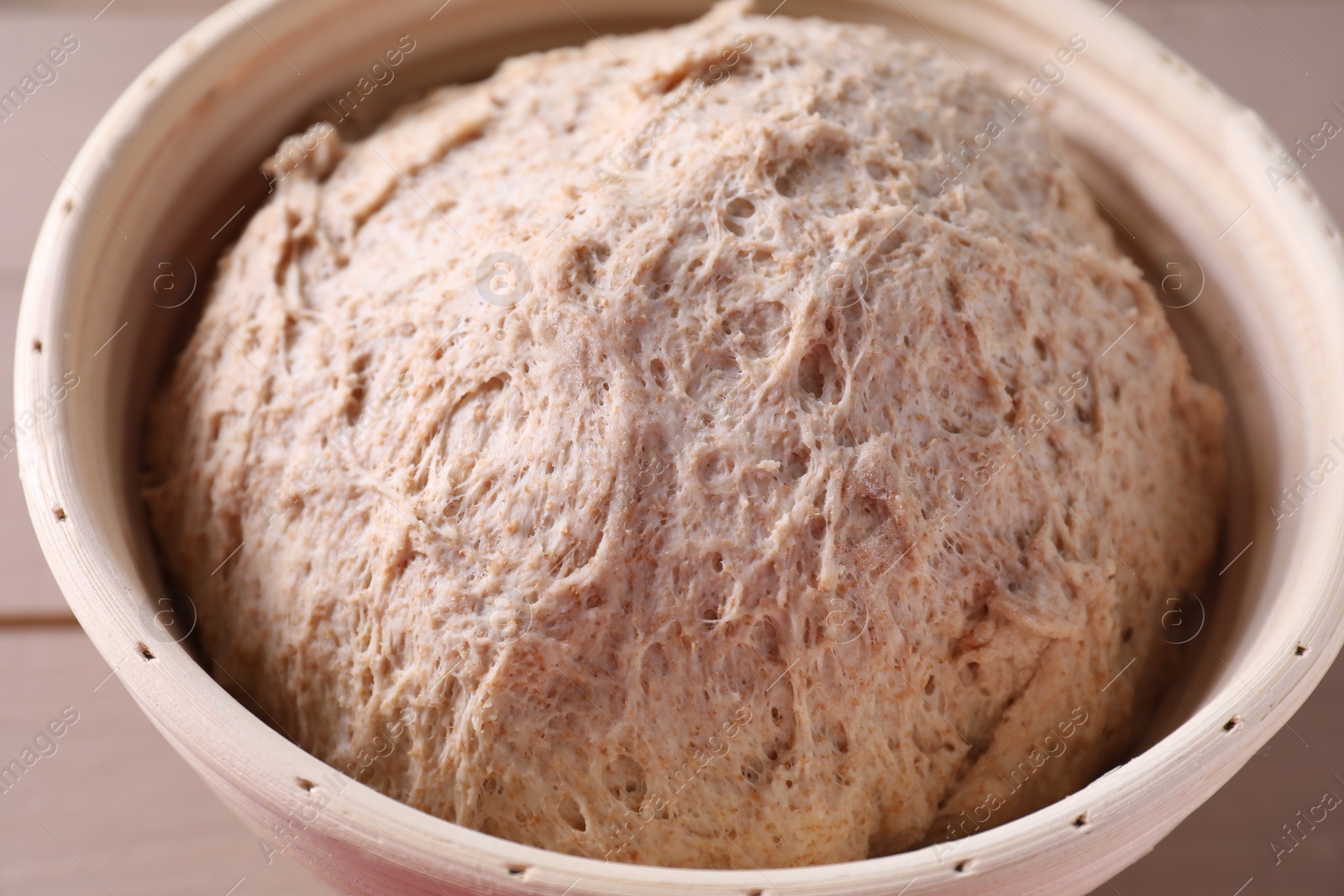 Photo of Fresh sourdough in proofing basket on table, closeup