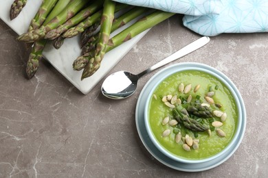 Delicious asparagus soup in bowl on grey marble table, flat lay