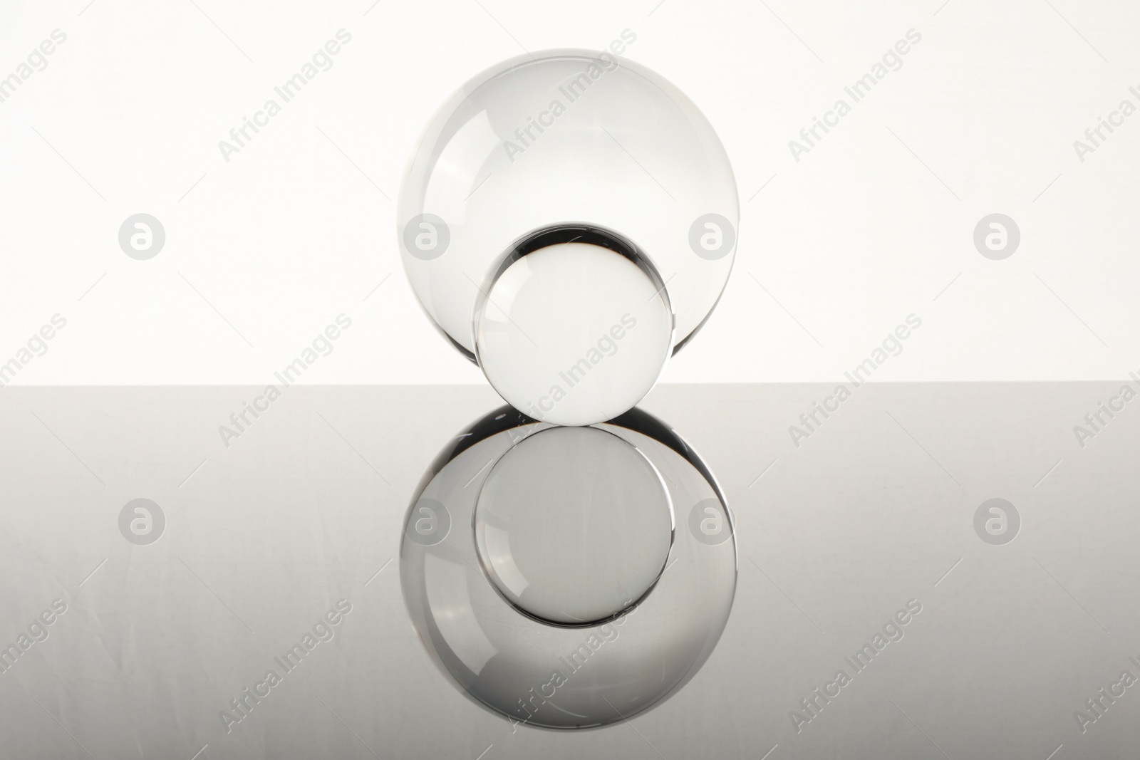 Photo of Transparent glass balls on mirror surface against light background