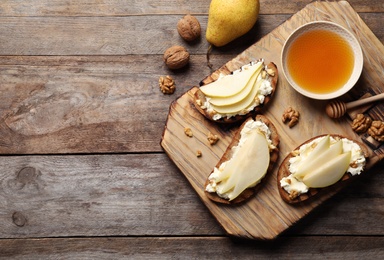 Toasted bread with tasty cream cheese and pear on wooden table, flat lay. Space for text