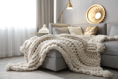 Photo of Cozy living room interior with knitted blanket on comfortable sofa