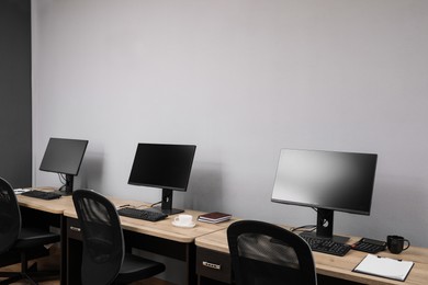 Photo of Open office interior. Modern workplaces with computers near light grey wall