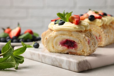 Tasty meringue roll with jam, cream, strawberry, blueberry and mint on light grey marble table, closeup