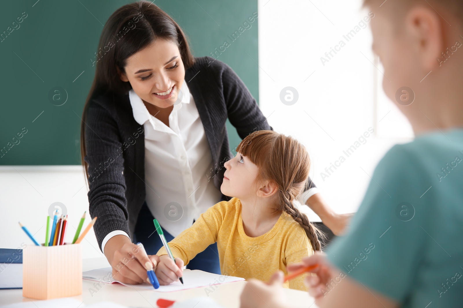 Photo of Female teacher helping girl with her task in classroom at school