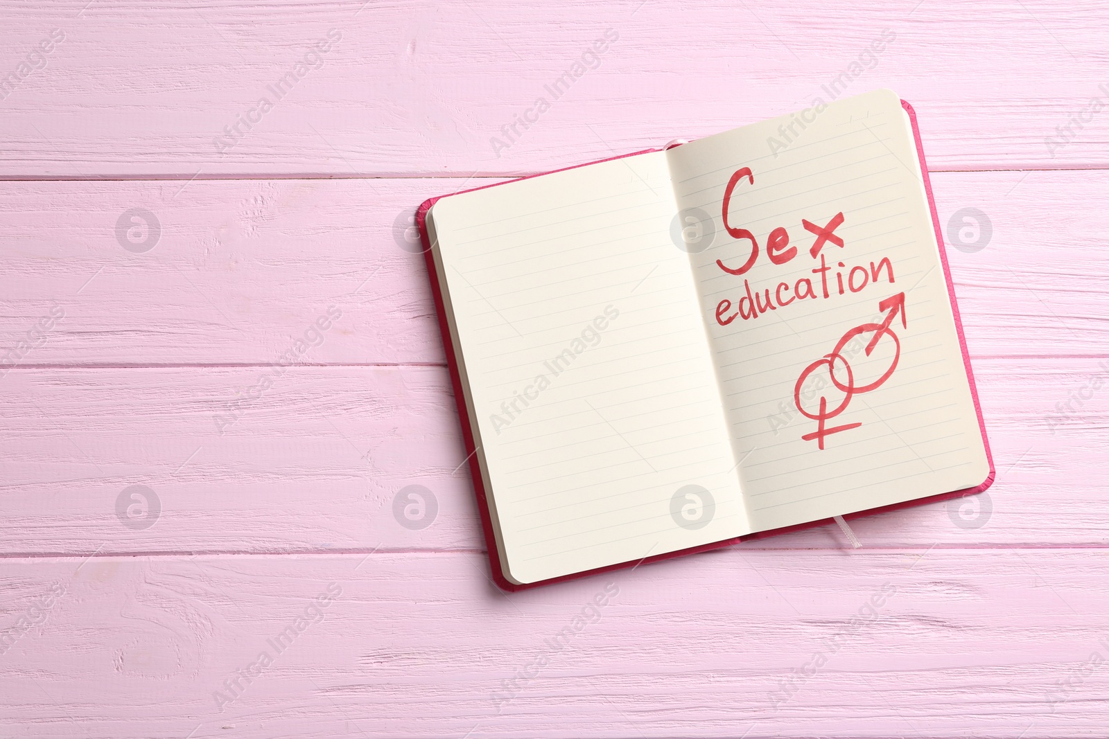 Photo of Notebook with phrase "SEX EDUCATION" and gender symbols on pink wooden background, top view. Space for text