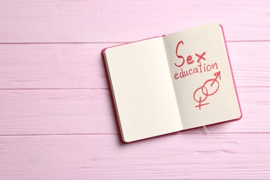 Notebook with phrase "SEX EDUCATION" and gender symbols on pink wooden background, top view. Space for text