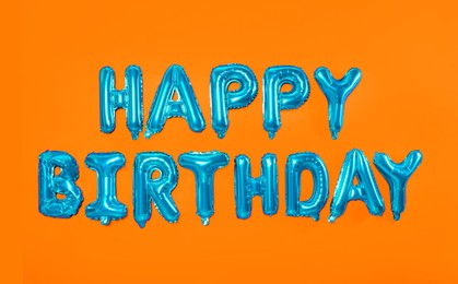 Image of Phrase HAPPY BIRTHDAY made of blue foil balloon letters on orange background