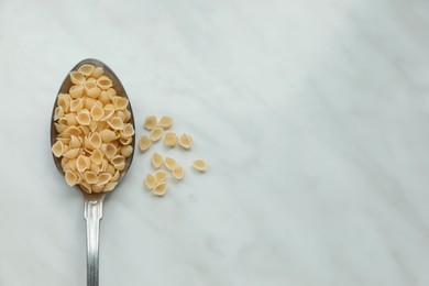 Photo of Spoon of uncooked conchiglie pasta on white marble table, flat lay. Space for text