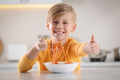 Photo of Happy boy eating tasty pasta at table in kitchen