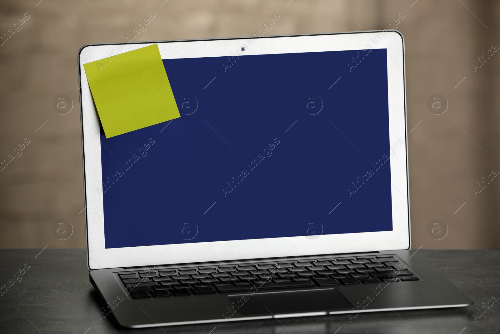 Photo of Laptop with blank sticky note on grey office desk. Space for text