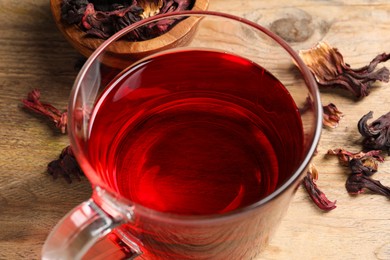 Cup of fresh hibiscus tea and dry flower leaves on wooden table, closeup