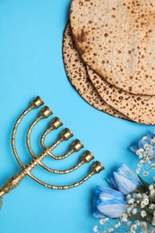 Photo of Tasty matzos, flowers and menorah on light blue background, flat lay. Passover (Pesach) celebration