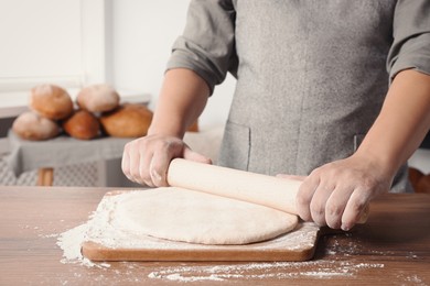 Photo of Man rolling dough at table in kitchen, closeup