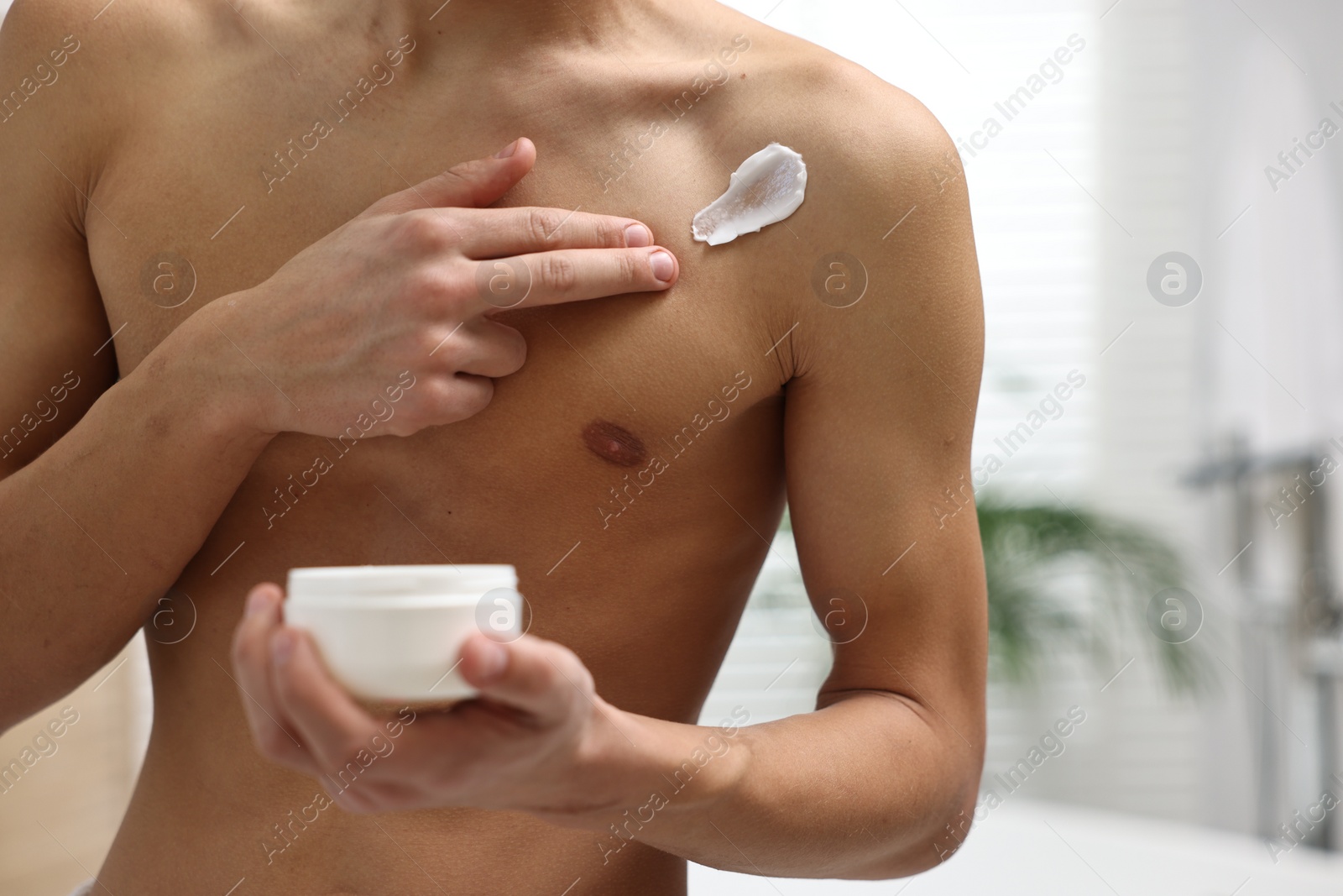 Photo of Man applying moisturizing cream onto his shoulder in bathroom, closeup