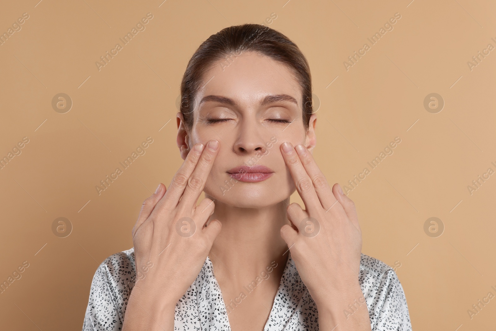 Photo of Woman massaging her face on beige background