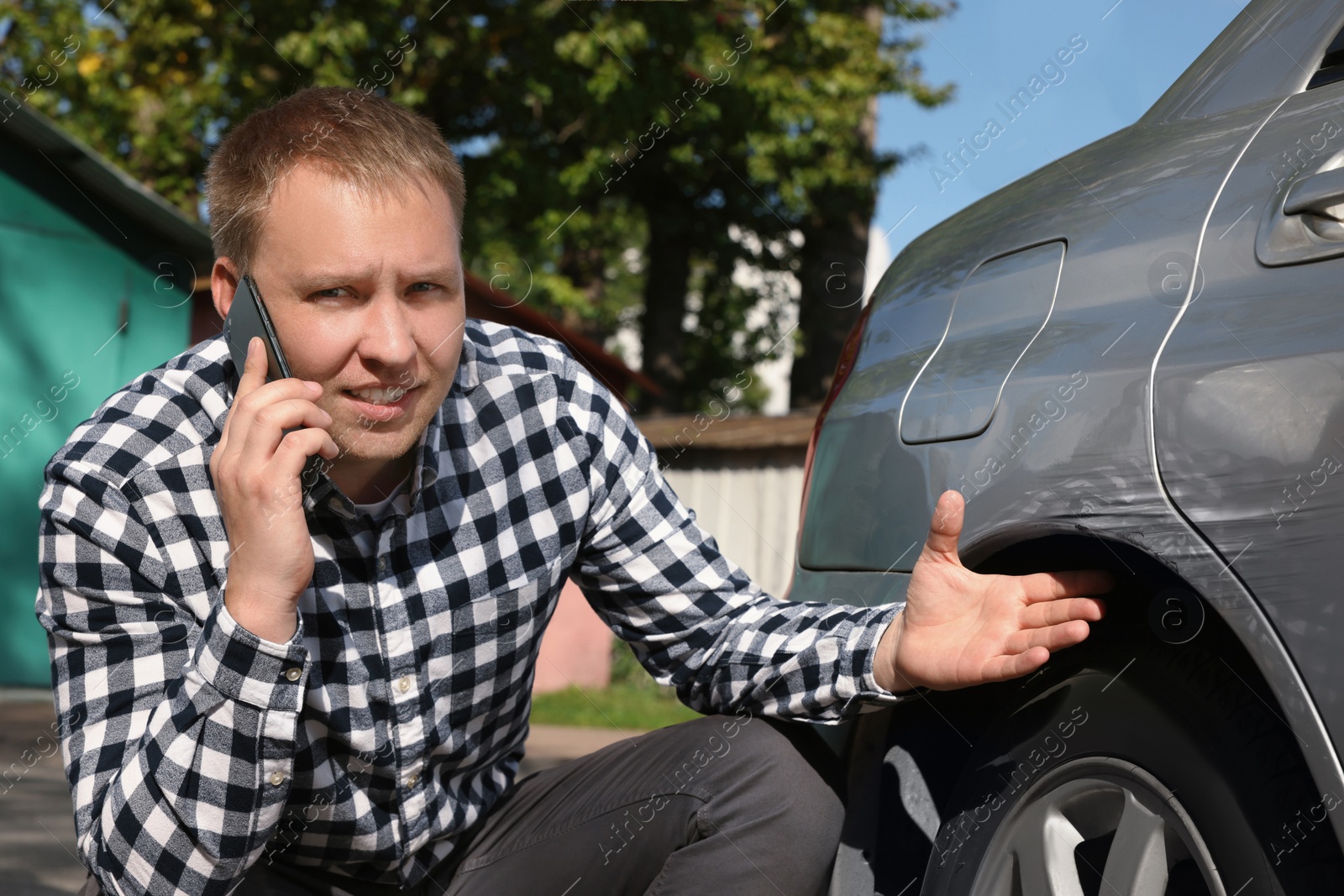 Photo of Man talking on phone near car with scratch outdoors