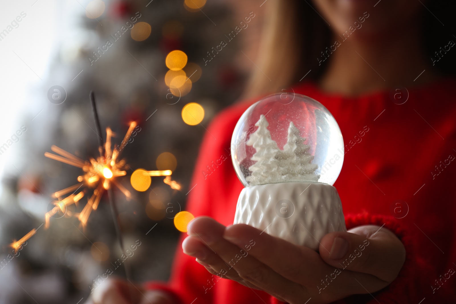 Photo of Woman with snow globe and sparkler near Christmas tree, closeup. Space for text