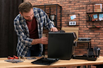 Photo of Man fixing coffee machine at table indoors