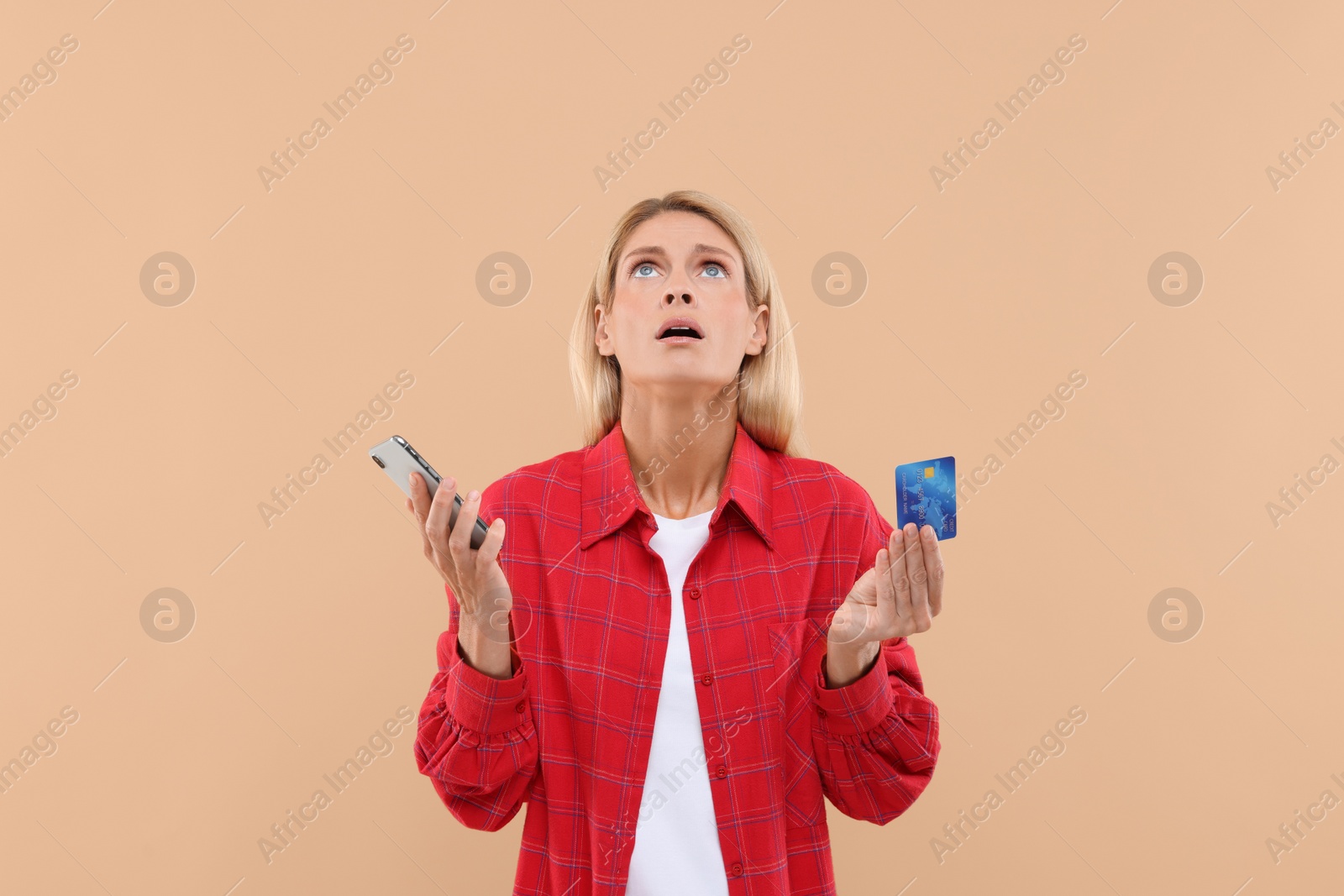 Photo of Emotional woman with credit card and smartphone on beige background. Be careful - fraud