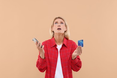 Photo of Emotional woman with credit card and smartphone on beige background. Be careful - fraud