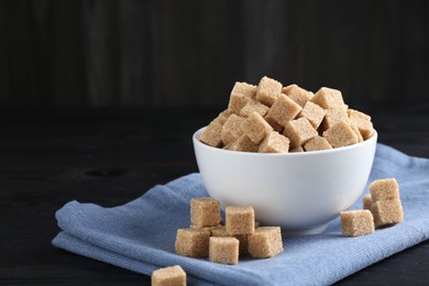 Photo of Brown sugar cubes on black wooden table, space for text