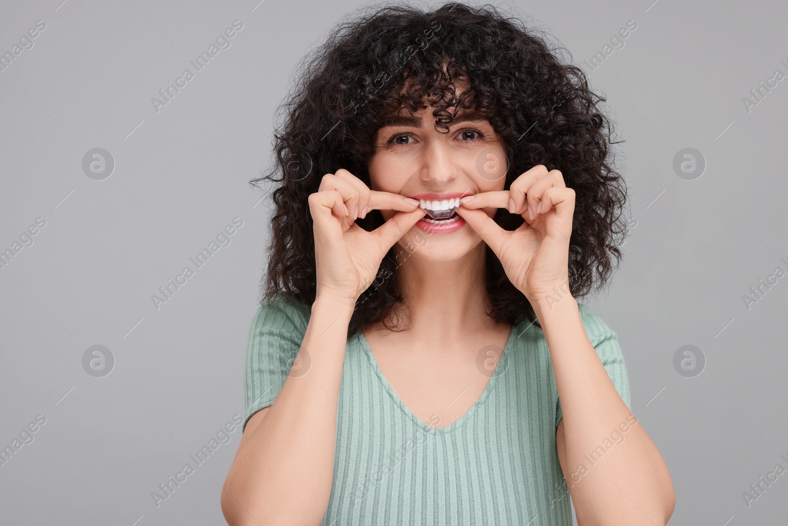 Photo of Young woman applying whitening strip on her teeth against grey background