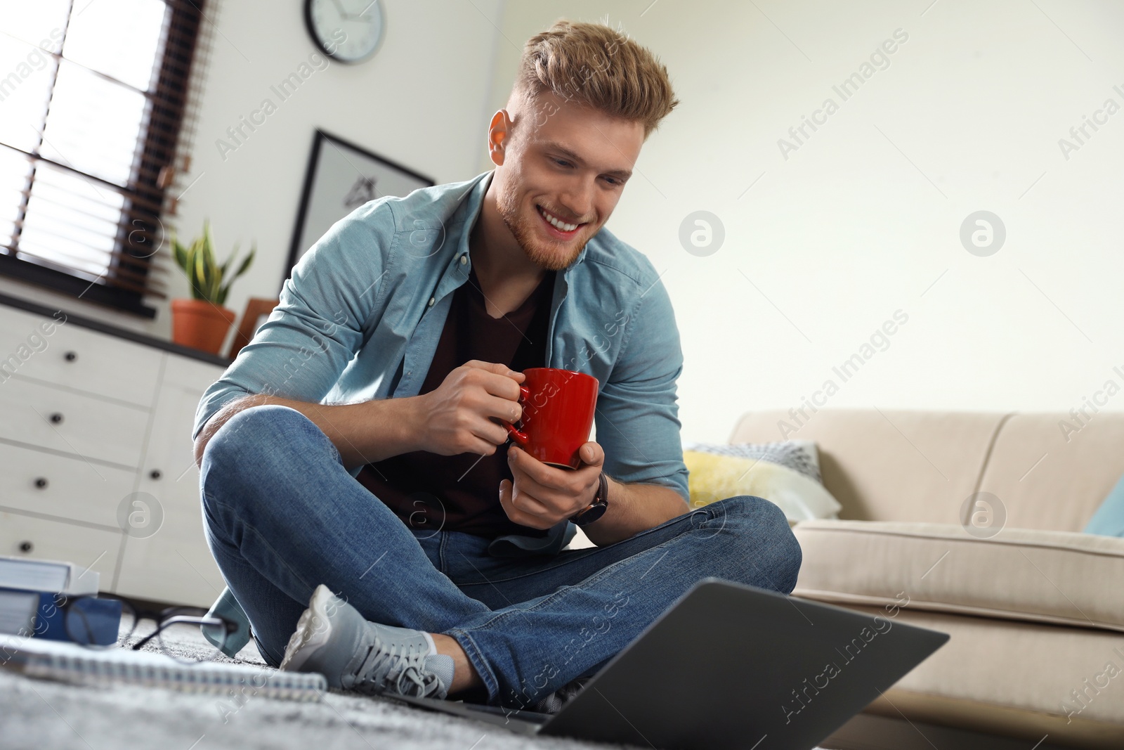 Photo of Young man using laptop while sitting on floor in living room